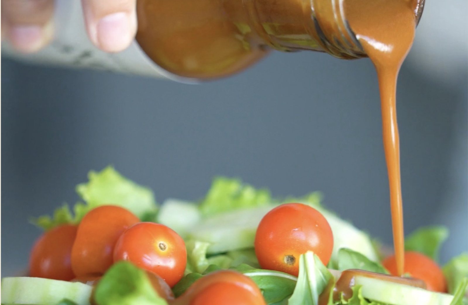 Vinagreta sirviéndose sobre una ensalada con jitomates cherry